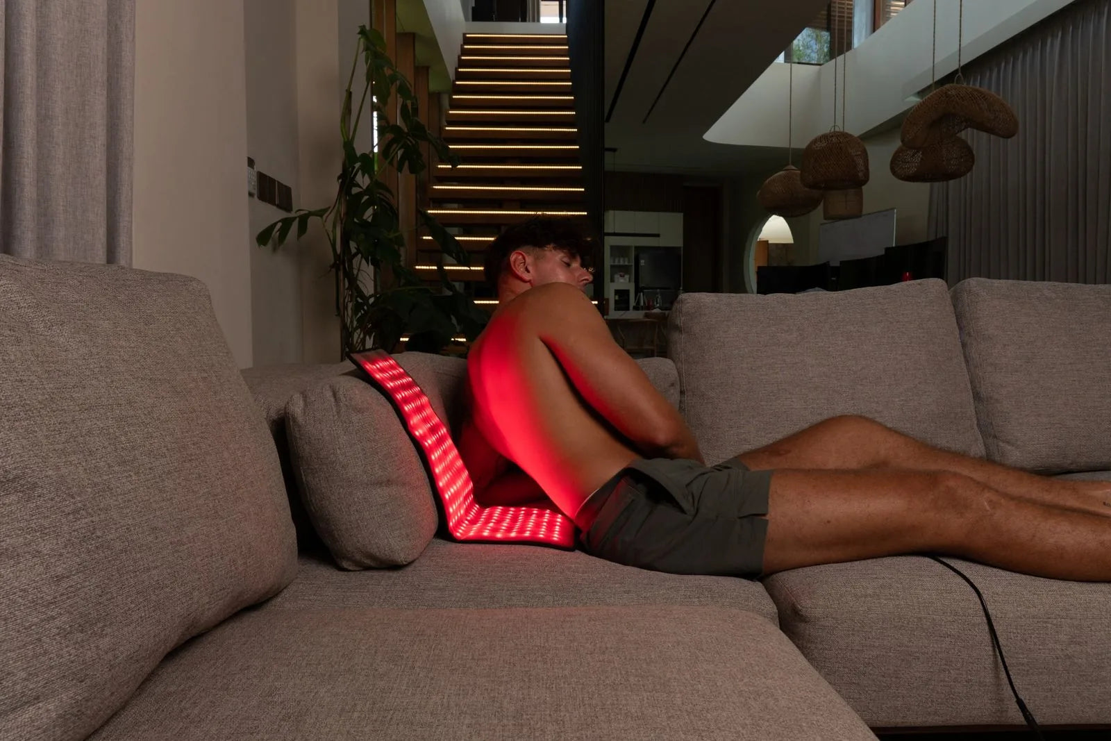 ThermoLab Auracell Pro red light belt glowing behind a man's lower back on a sofa